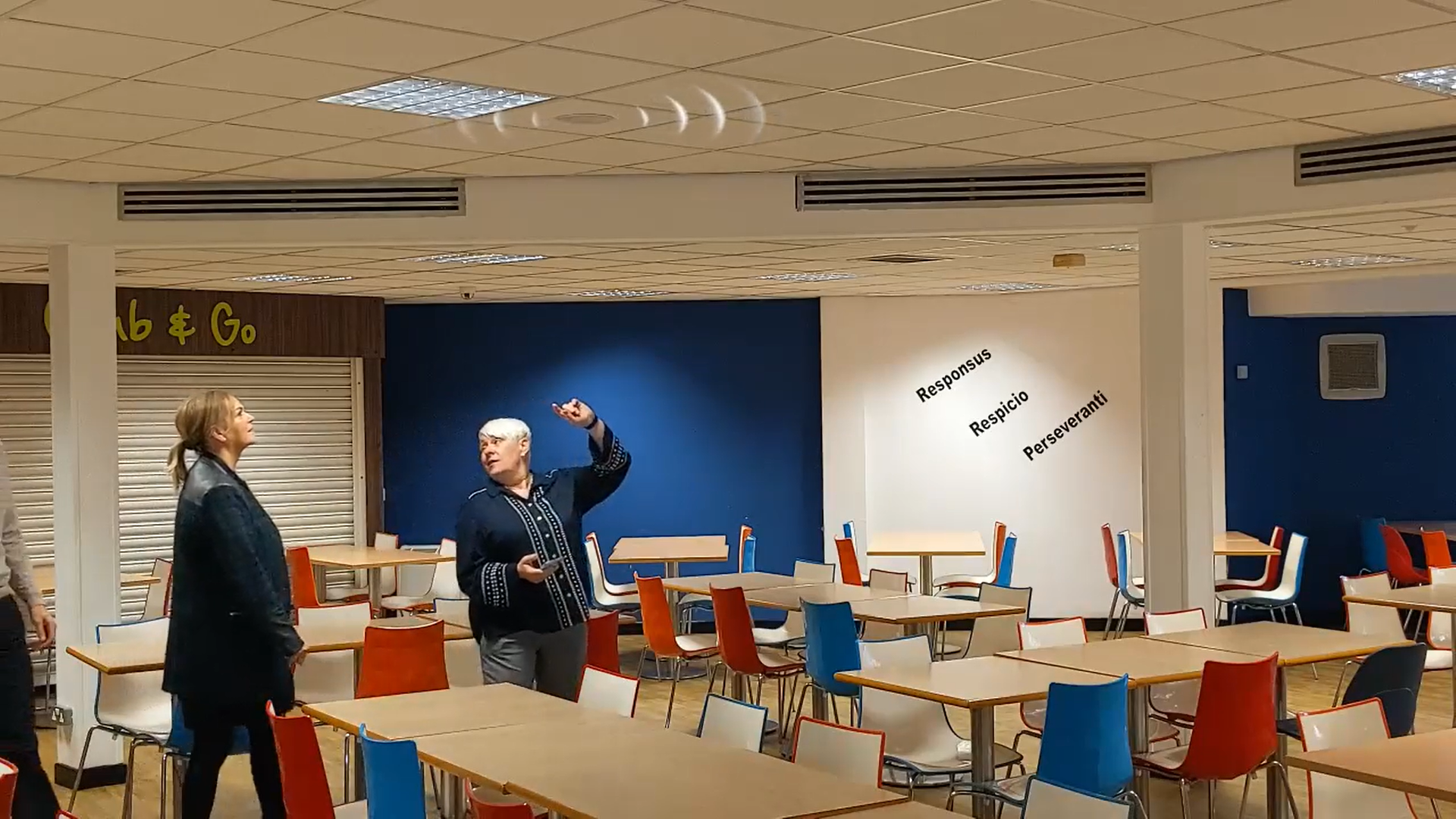 Headteacher Alicia Freeman pointing at a speaker in the canteen, discussing its effectiveness during peak times.