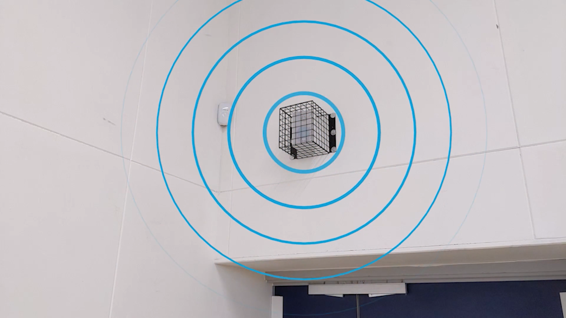 A speaker encased in a protective cage, mounted in the sports hall of The Heights School to shield it from potential impacts.